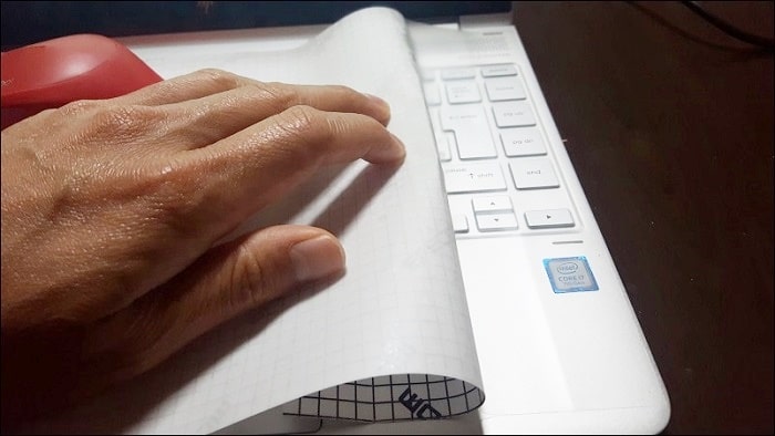 剥離紙から3分の1程度カバーを剥がしノートパソコンの端にあて、右手でしっかりと押さえて剥離紙をゆっくりと剥がしていく